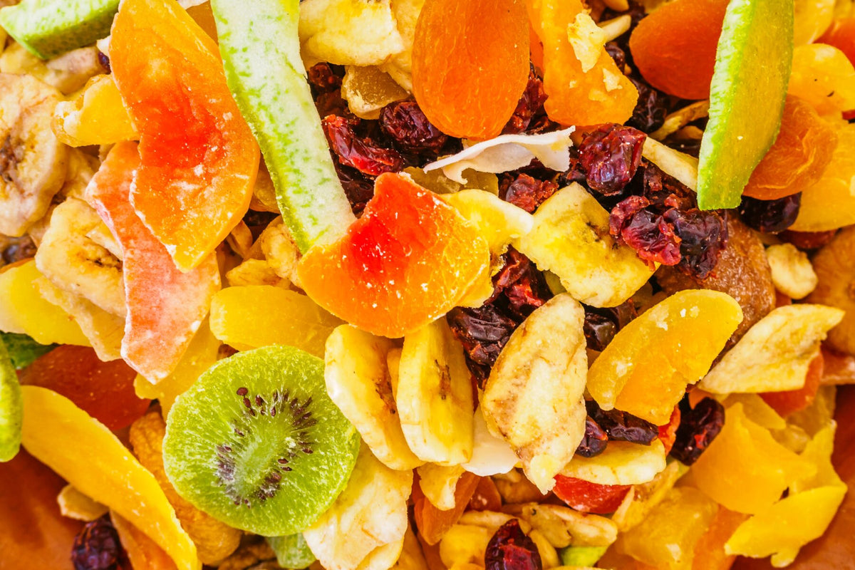 Verschiedene Trockenfrüchte wie Cranberrys, Feigen und Maulbeeren liegen in einer Schale auf einem Holztisch.